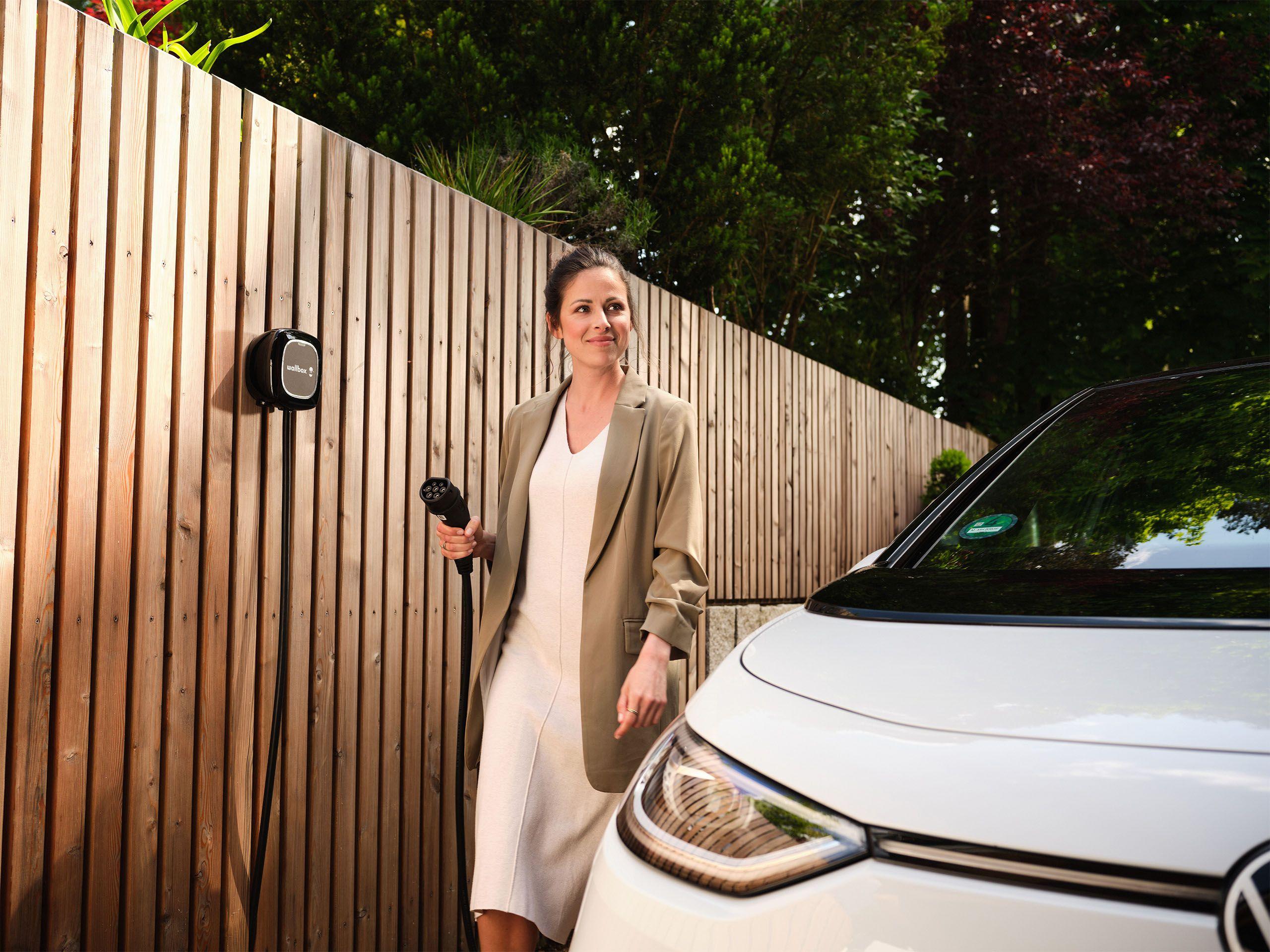 Frau steckt ihr E-Auto an die Wallbox