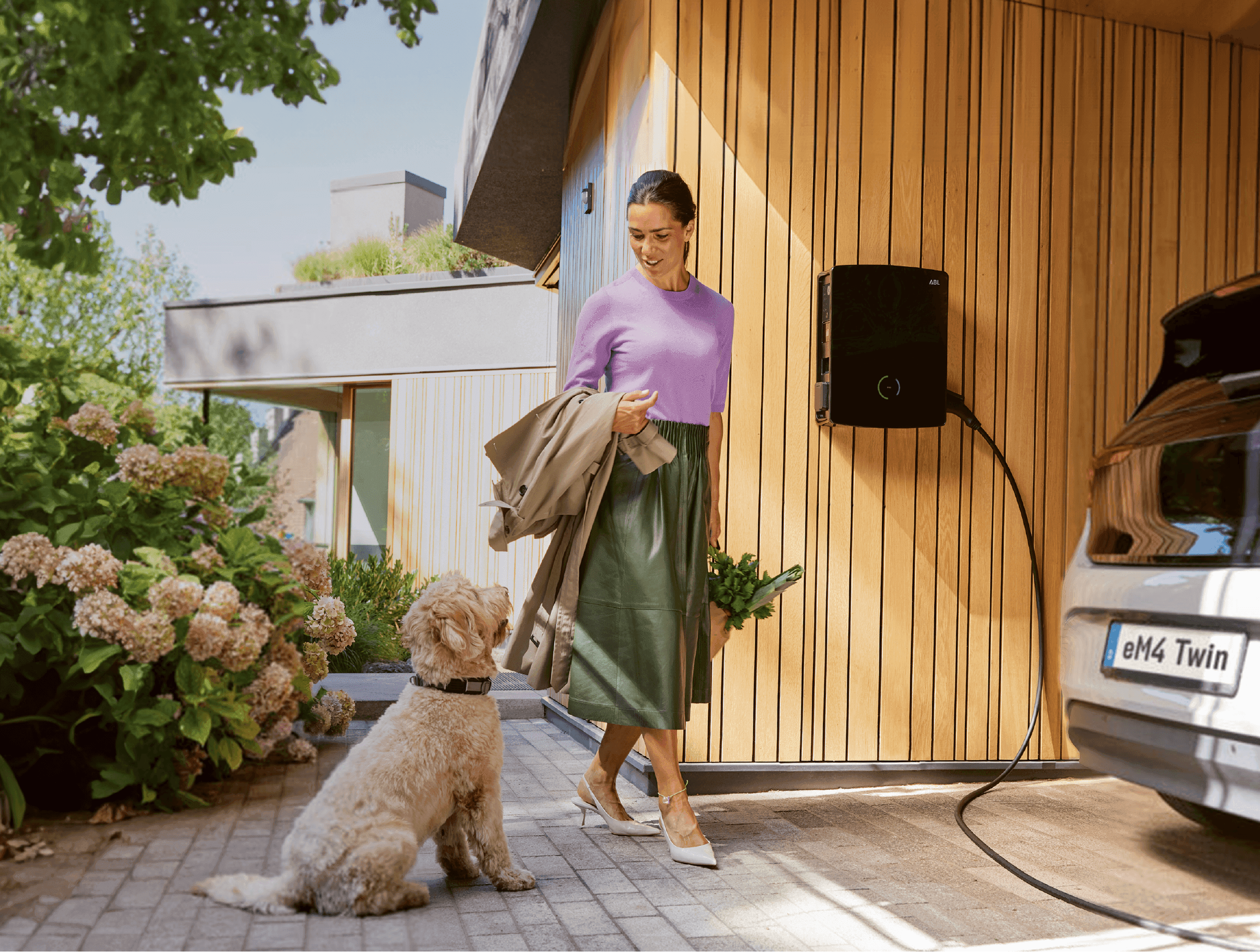 Frau und Hund stehen neben Auto, dass an der ABL Wallbox lädt