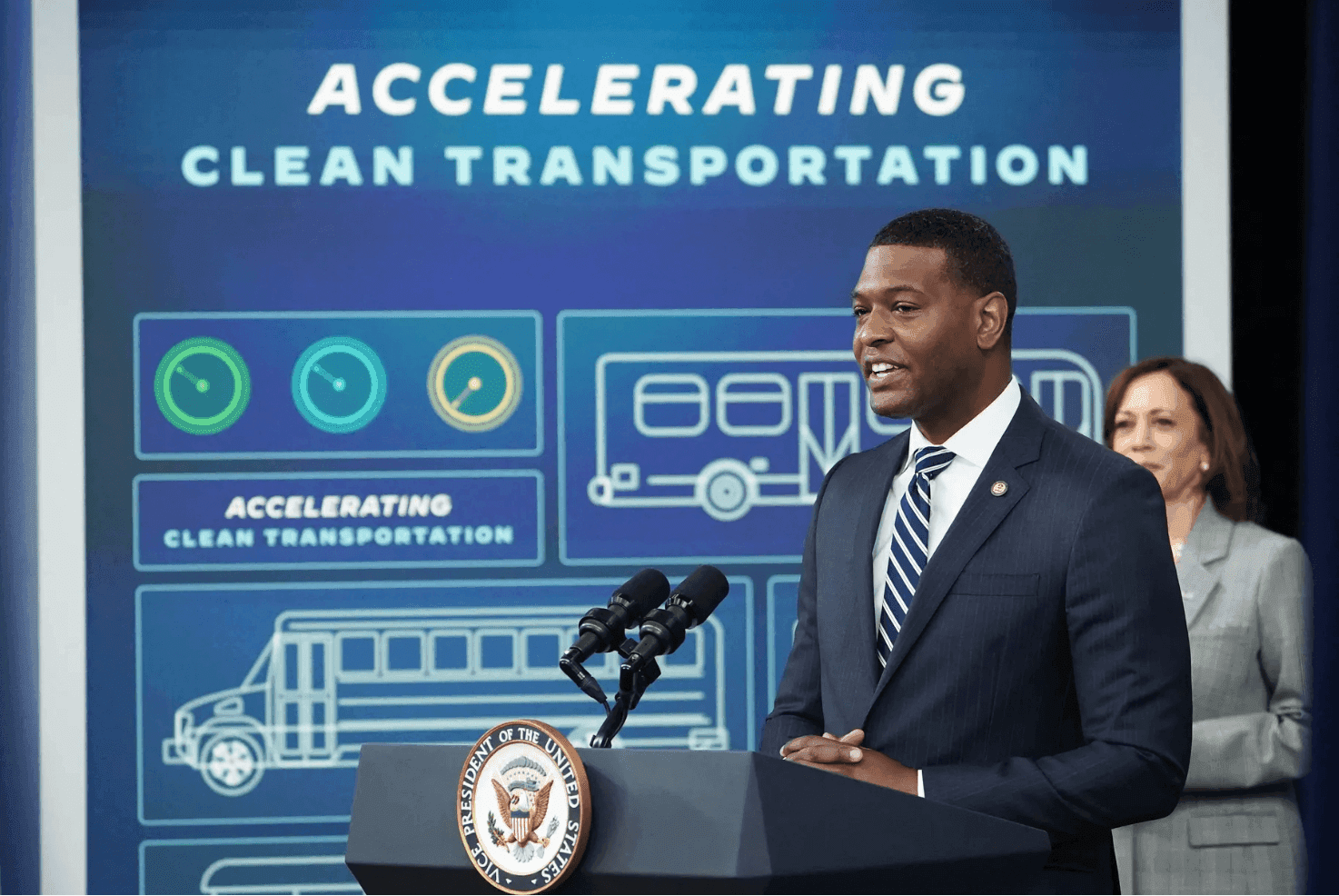 EPA Director Michael Regan speaks at a lectern, the text "Accelerating Clean Transportation" is seen behind him.
