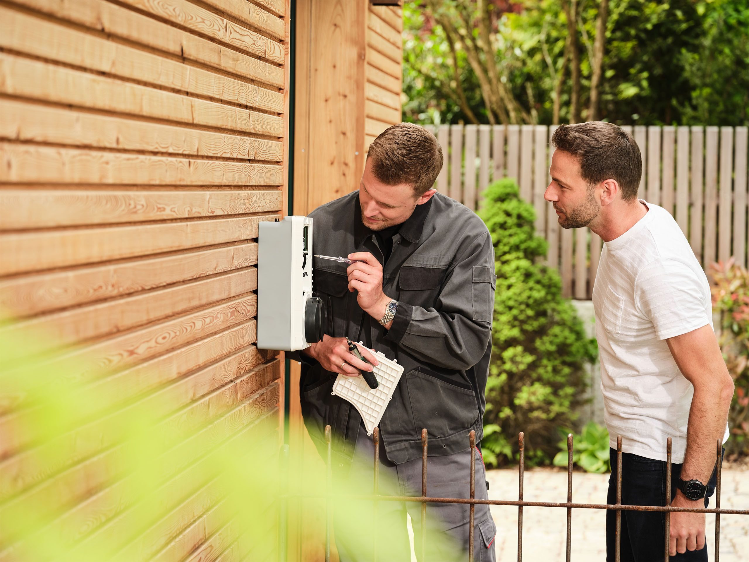 Elektriker montiert eine Ladestation, Kunde sieht zu