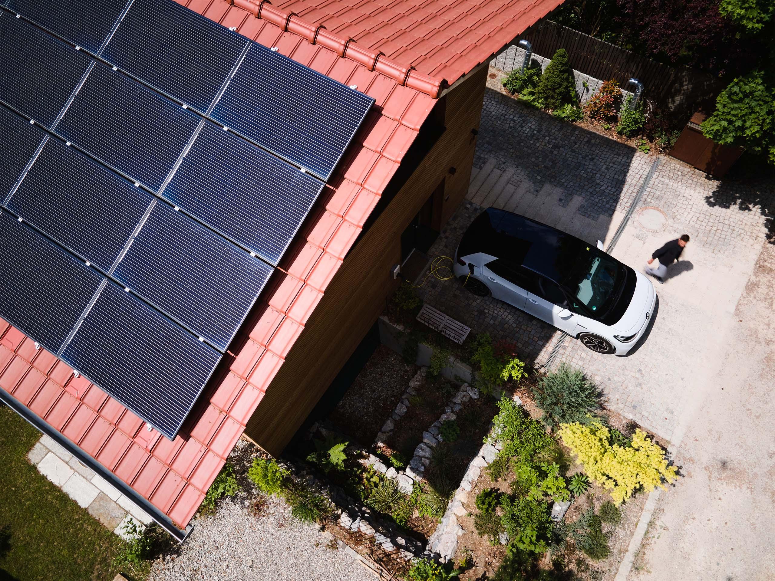 Vogelperspektive: E-Auto lädt vor einem Haus mit Solaranlage auf dem Dach