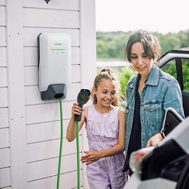 Frau und Kind steckt E-Auto an die Wallbox
