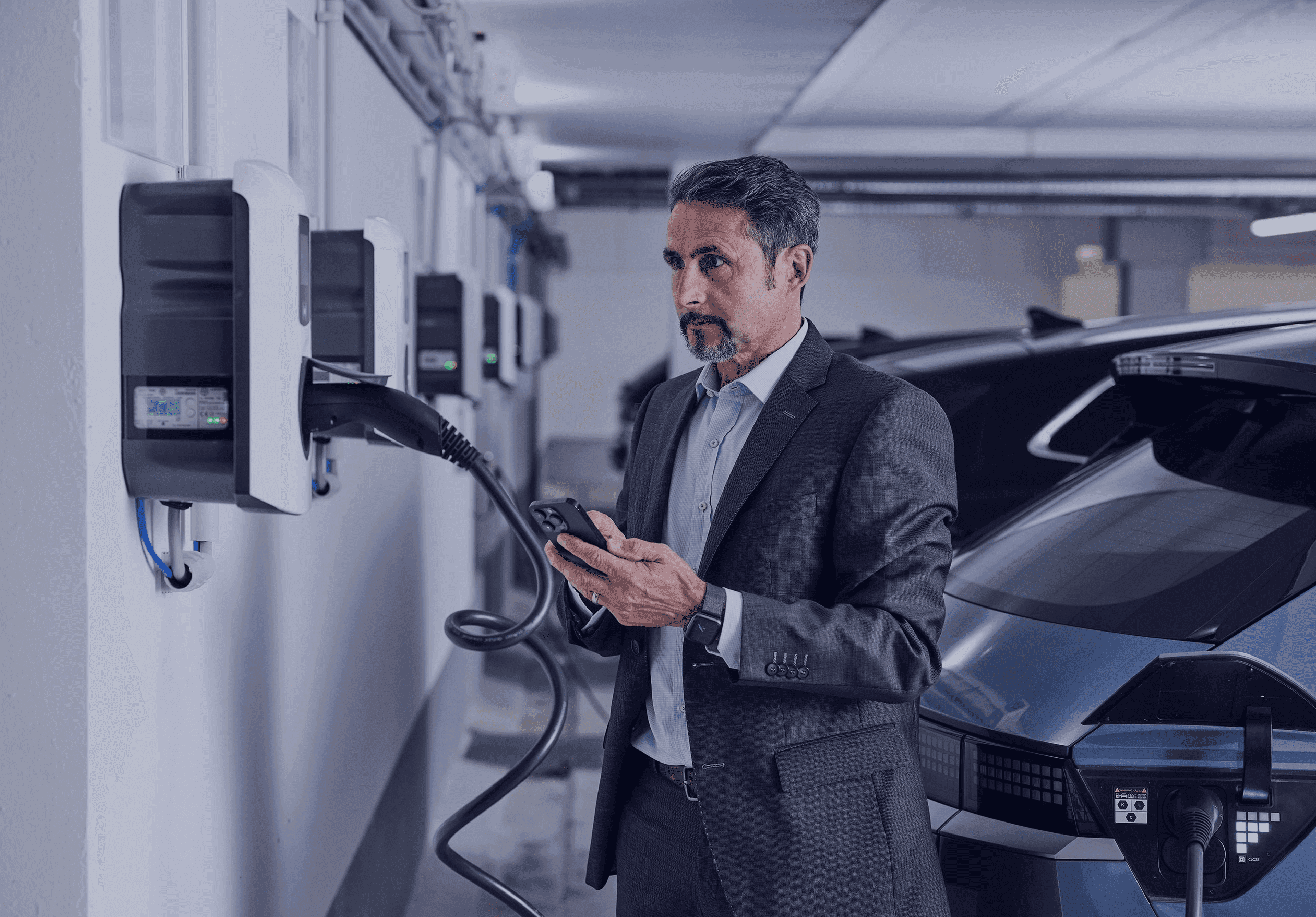 Mann steht mit seinem Handy vor der Wallbox in der Tiefgarage