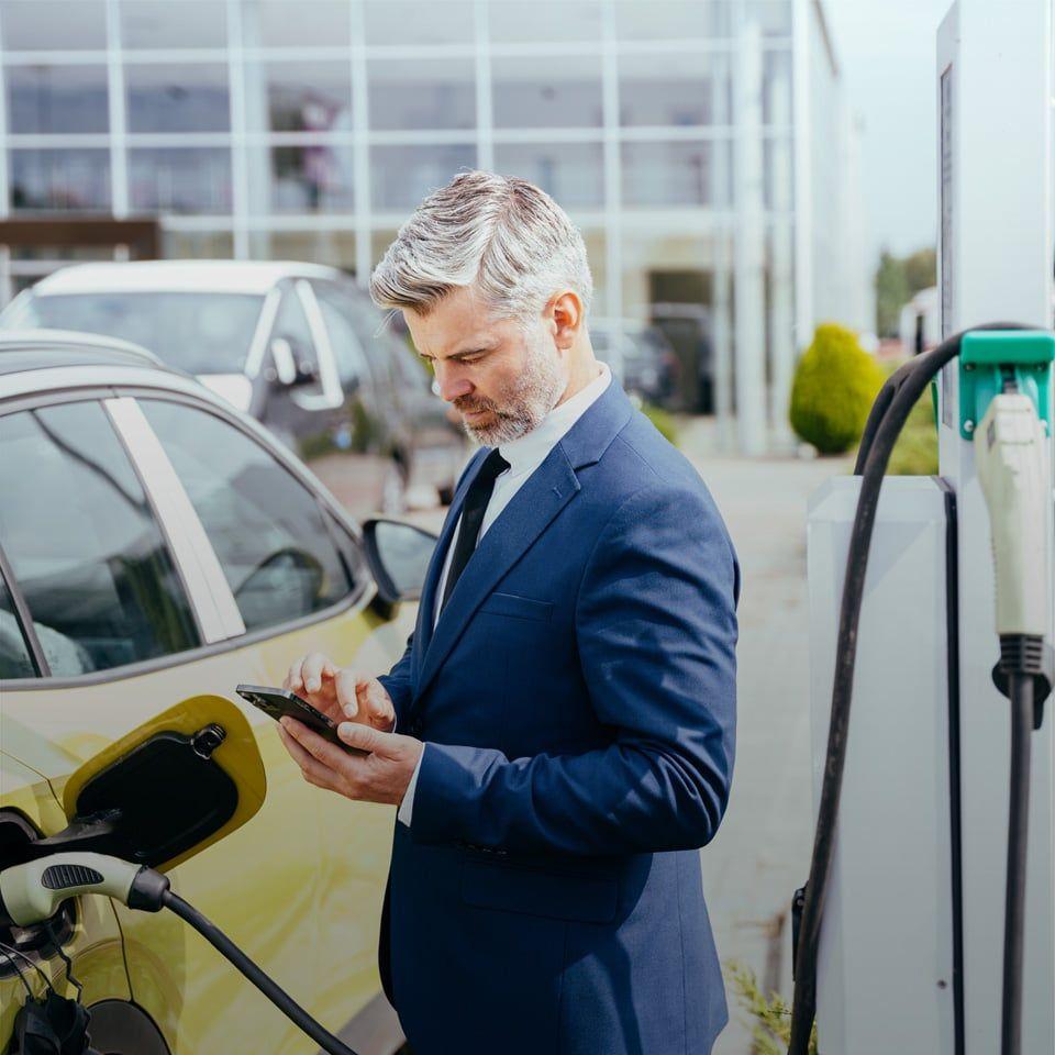 Mann im Anzug am Handy während sein Auto lädt