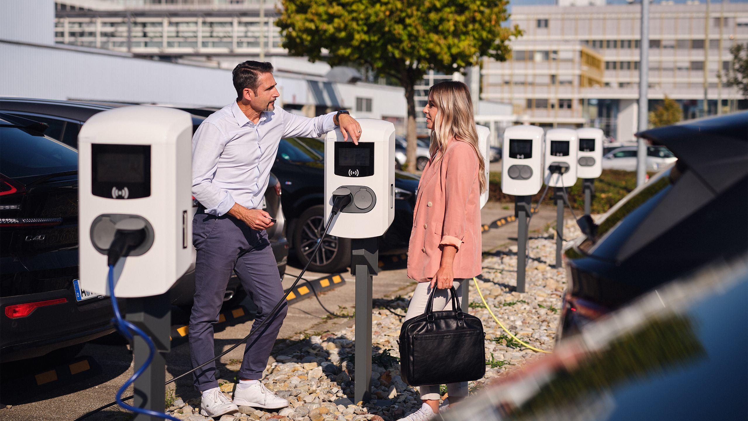 Kollegen unterhalten sich an Ladestation auf Firmenparkplatz 