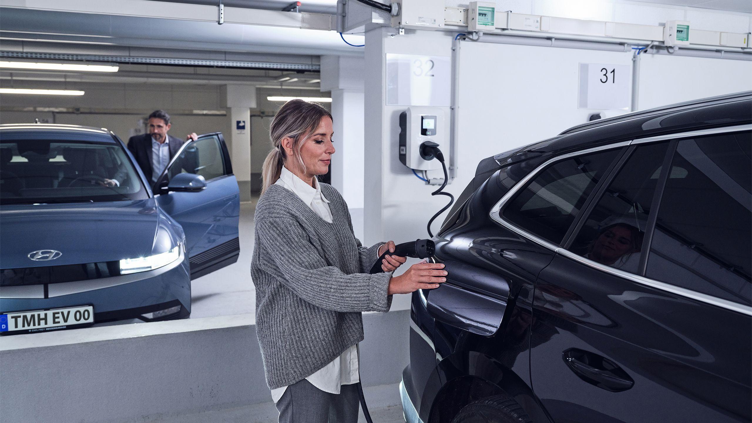 Frau steckt Ladekabel am Elektroauto an mit Kollege im Hintergrund