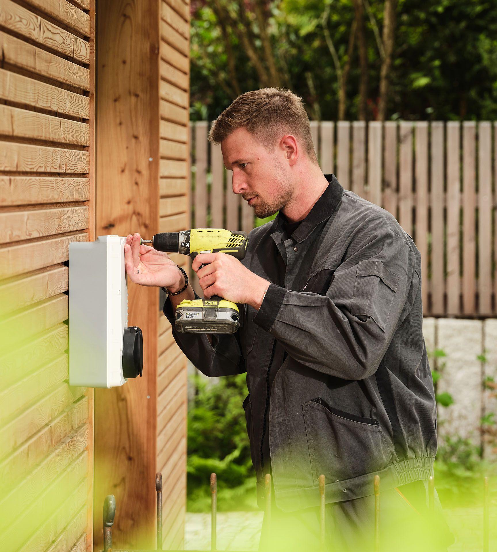 Ein Mann installiert eine Wallbox an einer Holzhaus