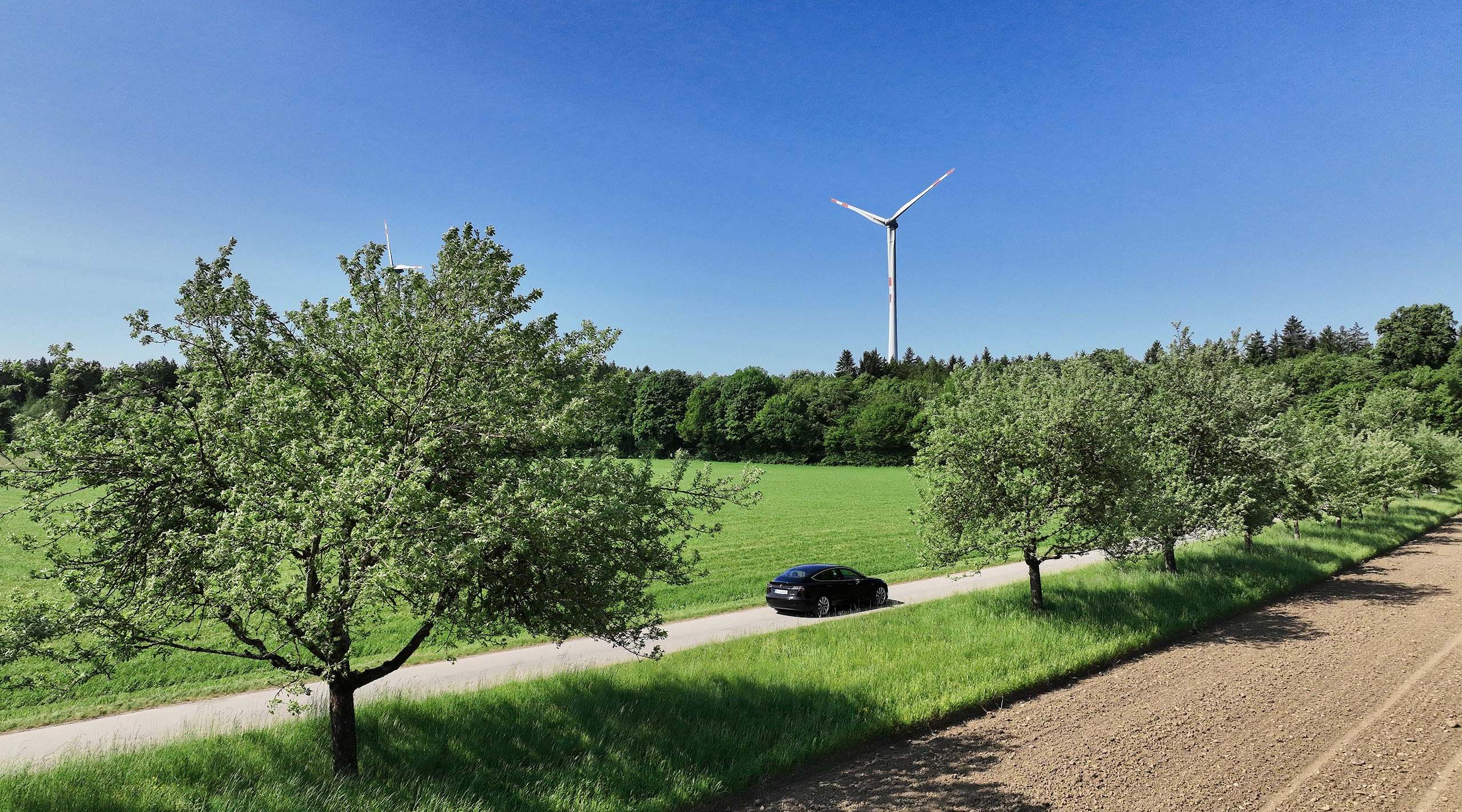 Landschaft mit fahrendem Elektroauto und einem Windrad