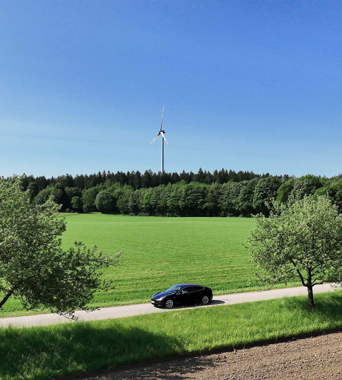 Landschaft mit Elektroauto vor Windraedern