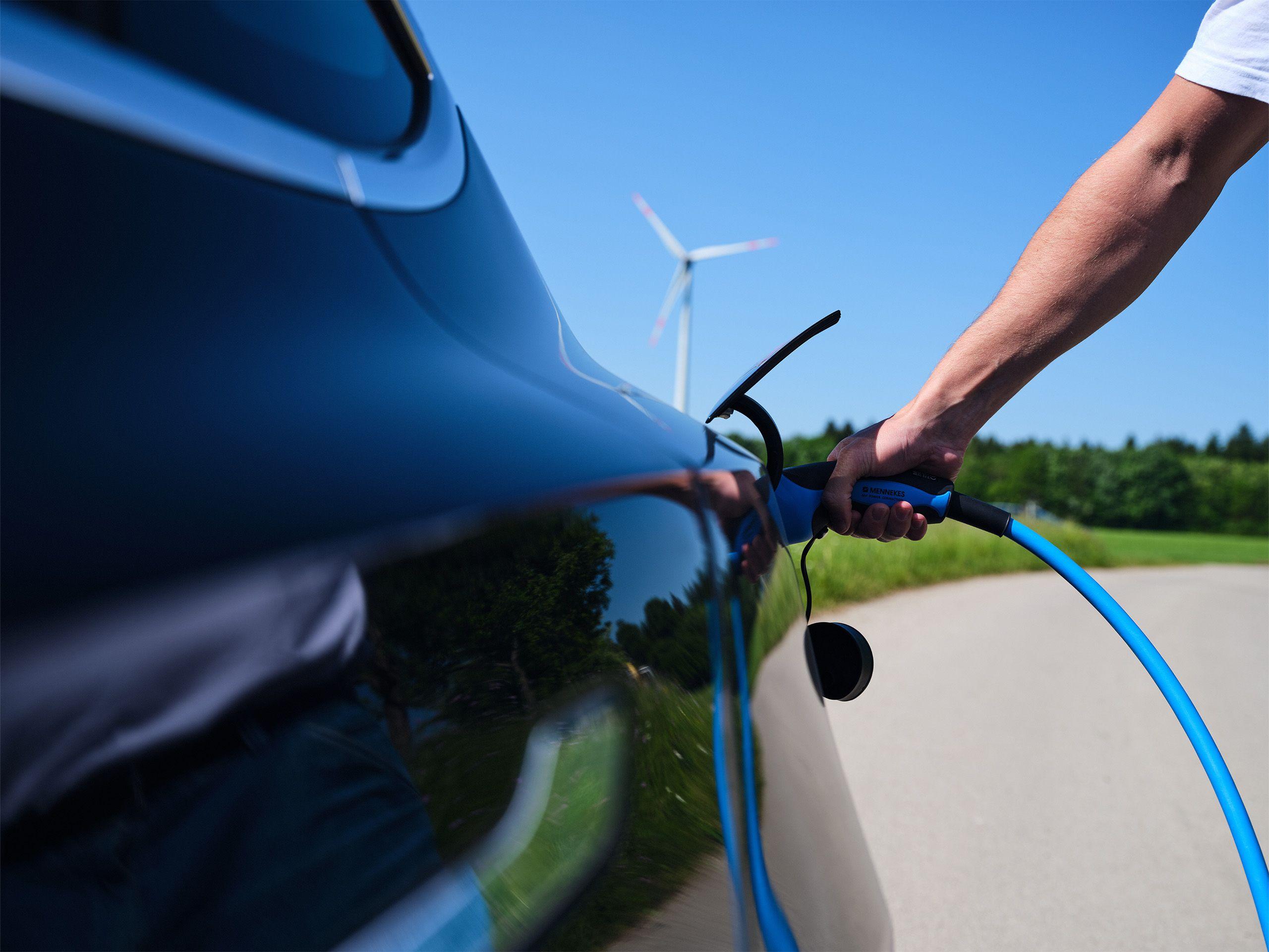 Ein Elektroauto wird geladen und im Hintergrund steht ein Windrad