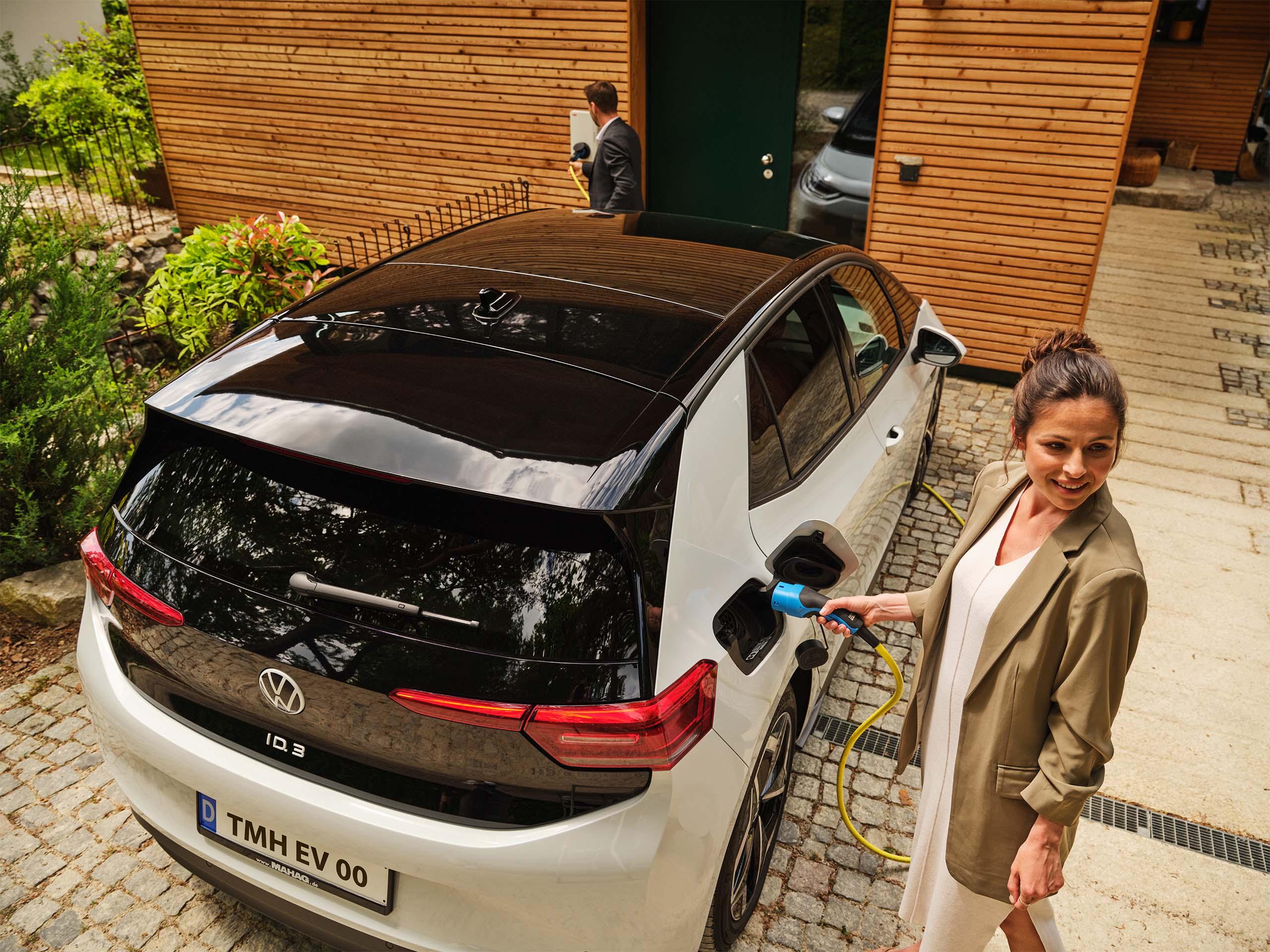 Eine Frau laedt ihr Elektroauto vor ihrem Haus