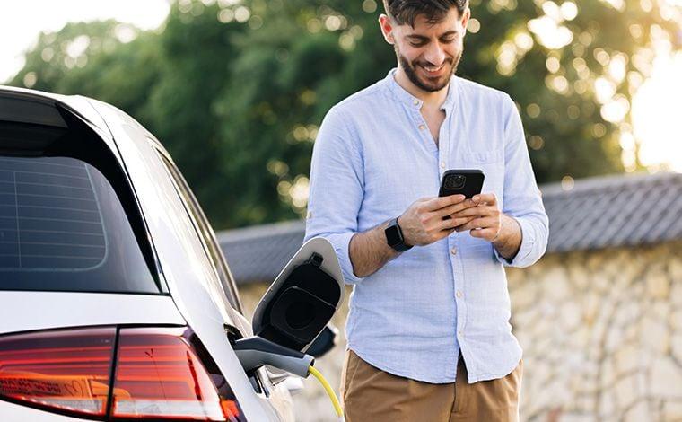 Young man on cell phone while charging e-car