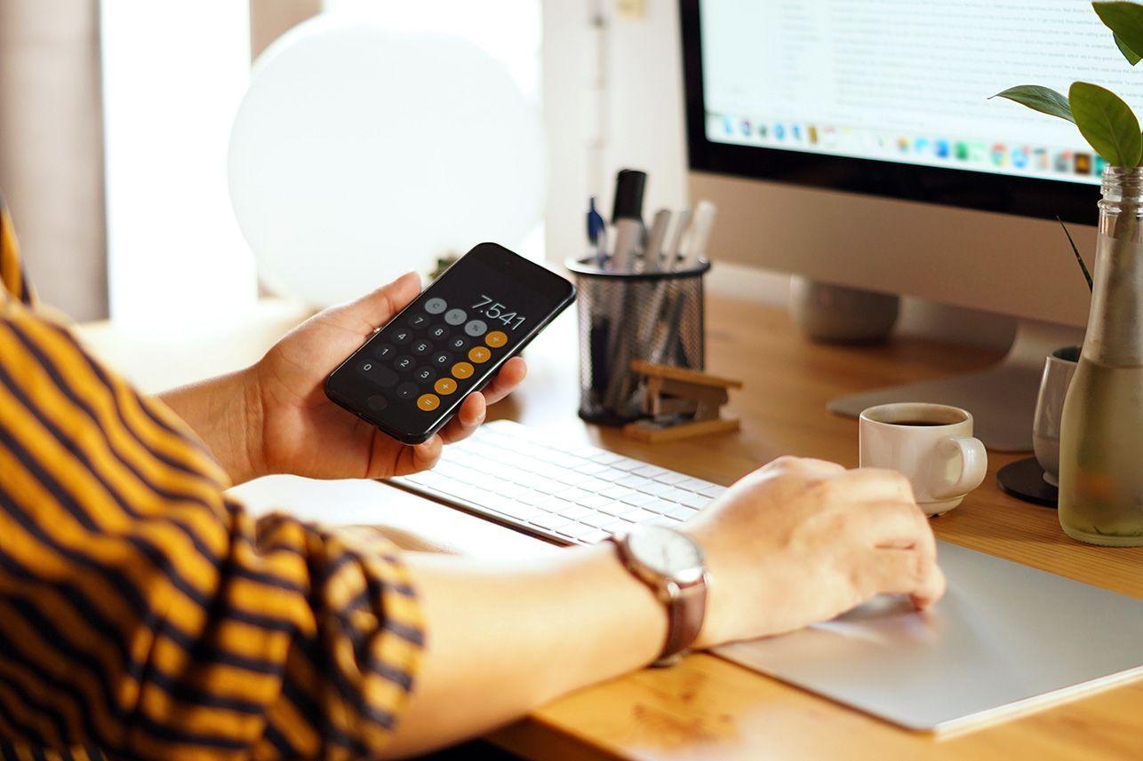 Frau rechnet am Taschenrechner vor dem PC
