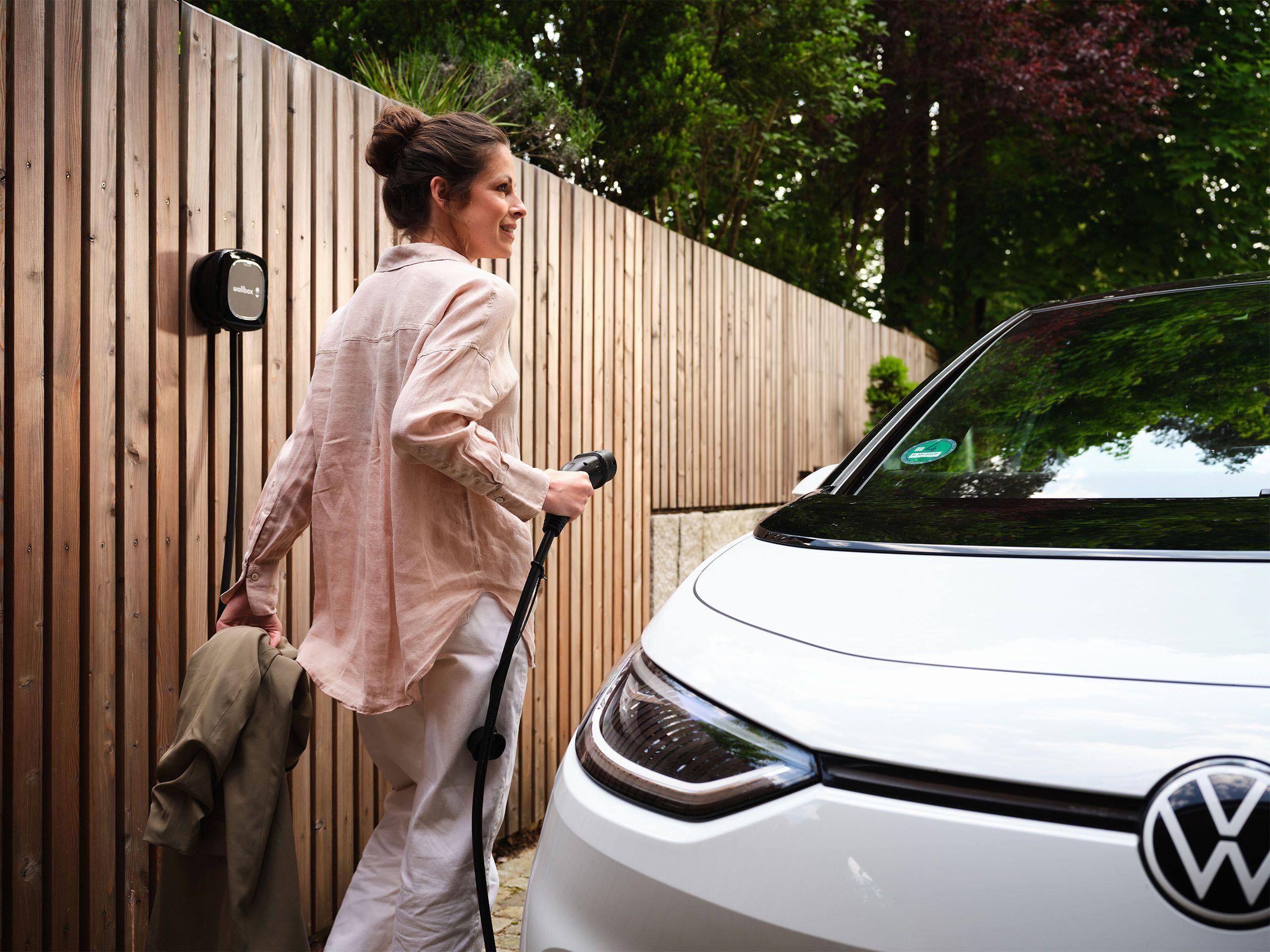 Frau steckt ihr E-Auto in der Einfahrt an