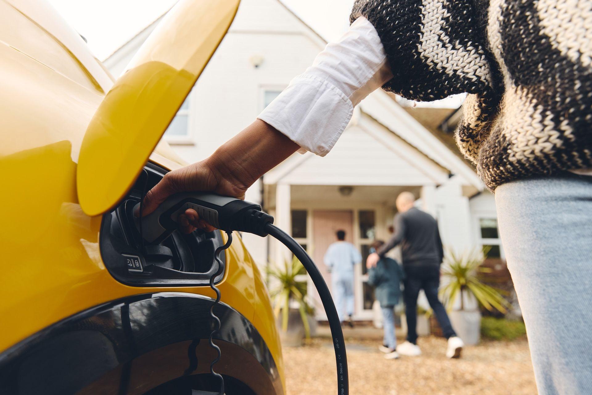 Woman plugging in electric vehicle outside of her home