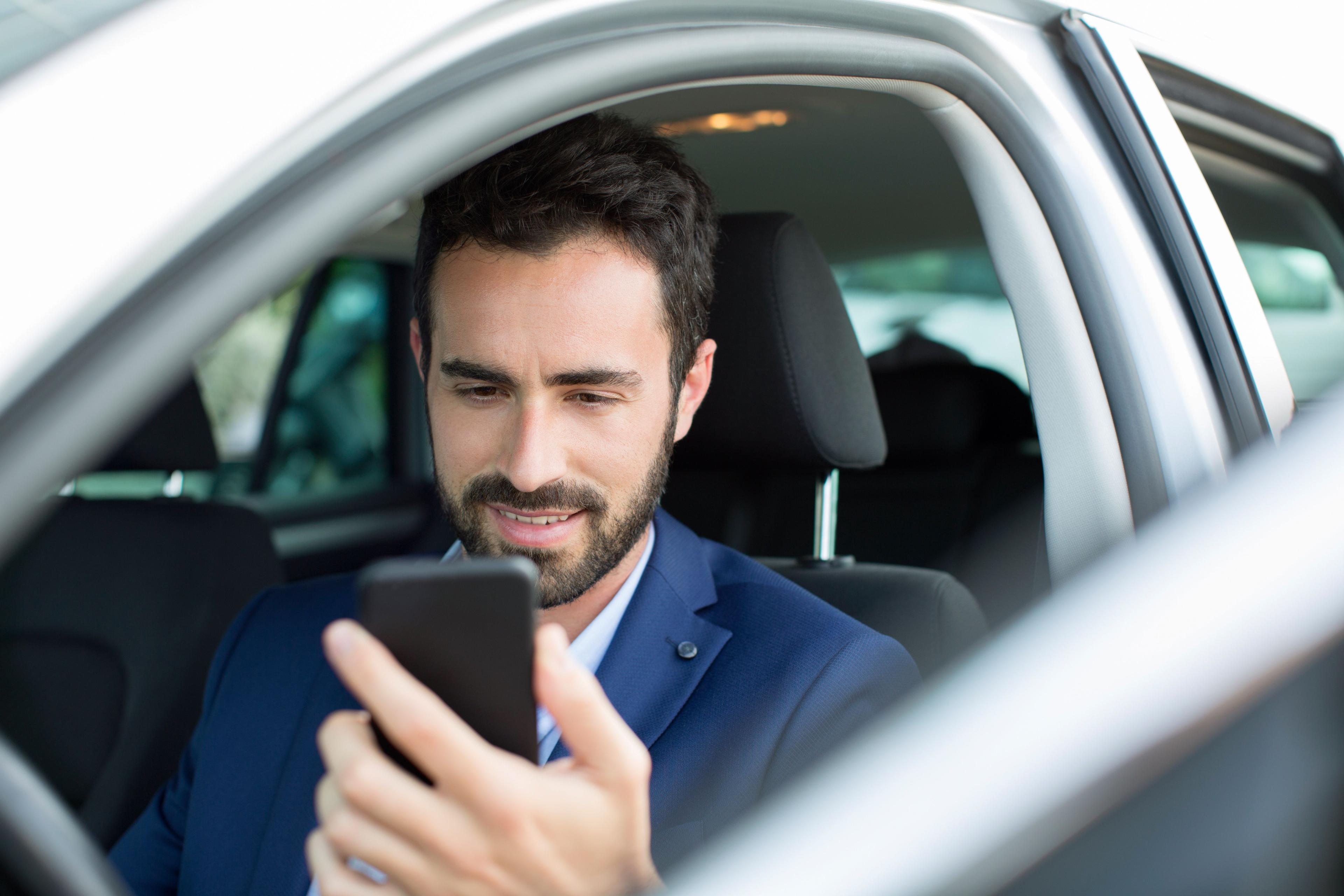 Mann sitz im Auto und schaut auf sein Handy